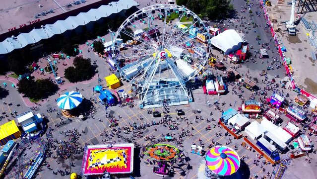 aerial hold top view worlds largest portable Ferris Wheel at 150 feet high drone overlooking birds eye view of the rides line ups of crowds of people at swings go karts mega drop lots more fun times