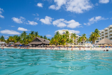 Naklejka na ściany i meble People swimming near white sand beach with umbrellas, bungalow bar and cocos palms, turquoise caribbean sea, Isla Mujeres island, Caribbean Sea, Cancun, Yucatan, Mexico