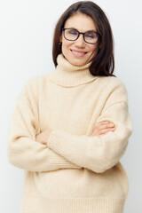 Fototapeta premium A sweet, beautiful, intelligent woman in a stylish beige sweater, stands with glasses for vision with her arms crossed on her chest
