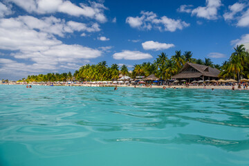 People swimming near white sand beach with umbrellas, bungalow bar and cocos palms, turquoise caribbean sea, Isla Mujeres island, Caribbean Sea, Cancun, Yucatan, Mexico
