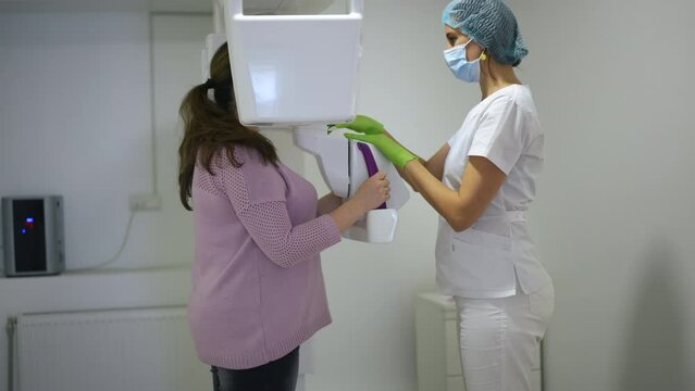 Side view professional doctor using dental cone beam scanner examining plus-size woman in hospital. Expert Caucasian dental assistant doing teeth and jaw tomography for patient in slow motion