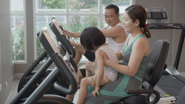 Family with father and mother and son riding bike exercise for health and bodycare together in the fitness gym, dad and mom and boy doing activity for wellbeing and care, lifestyles concept.
