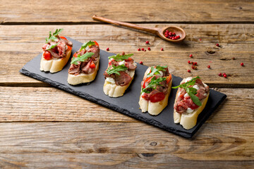 Bruschetta with roast beef, tomatoes and aragula on black stone