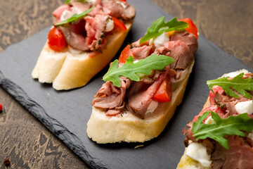 Bruschetta with roast beef, tomatoes and aragula on black stone