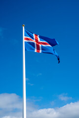 Selfoss, Iceland - July 2, 2022 Vertical view of the Icelandic flag waving from a flag pole at Thingvellir National Park. Composed of a blue field and white-edged red Nordic cross.