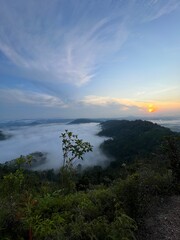 sunset over the mountain hill in tropical climate with fog covering the hills