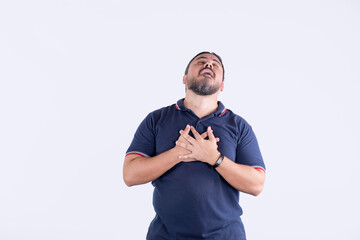 A middle aged man letting off a sigh of relief. Grasping his chest and looking up. Isolated on a white backdrop.