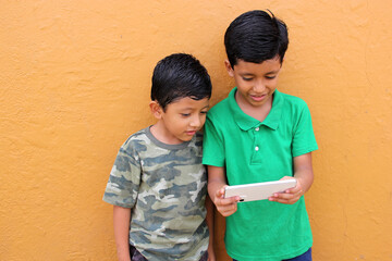 Two dark-haired Latino male children living in poverty use their cell phones to play games and are...