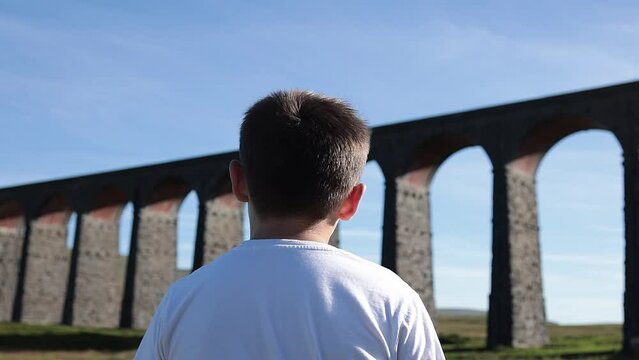 Boy standing and looking out over a large arched railway bridge. Ribblehead Viaduct or Batty Moss Viaduct