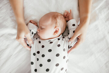 Newborn baby sleeps calmly and sweetly on the bed holding his mother's hands