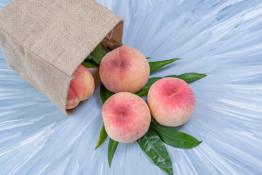 Fresh Sweet Peach on blue wooden  background, Pink and yellow Peach fruit with leaf with natural color cloth bagt.