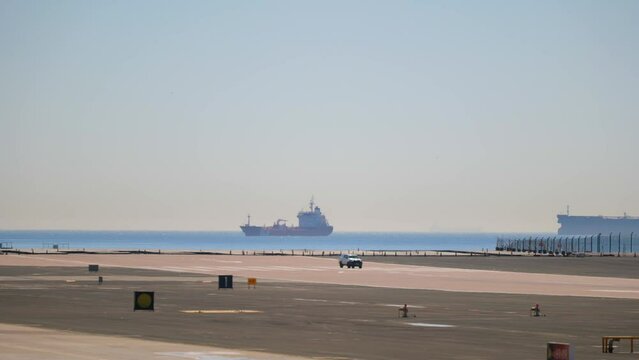 Wide View Of Gibraltar International Airport With Follow-Me Car Driving On Airfield. Ship On Seascape In Background.