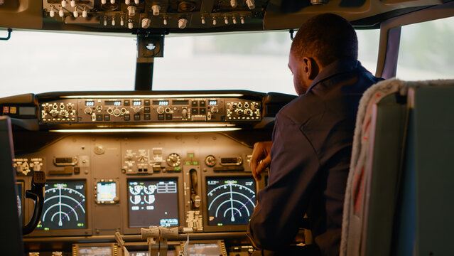 African american captain inserting destination coordinates to help pilot before takeoff, flying airplane with dashboard command. Using control panel buttons, windscreen compass and radar.