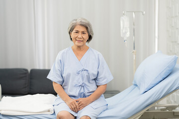 Fototapeta premium Senior asian woman sitting on bed with receiving saline solution from bag at hospital ward. medicine, health care, old people and quarantine concept