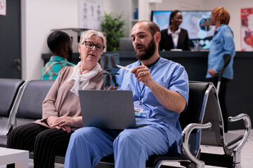 Healthcare assistant showing x ray to senior patient, sitting in hospital reception lobby. Nurse explaining radiography scan results to woman with disease, talking about treatment and diagnosis.