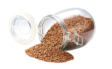 Raw buckwheat spill out of a glass storage jar isolated on white background.