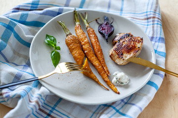 Glazed and roasted young red beet, carrots with baked chicken on a plate on the towel on the wooden background. Roasted vegetables with rosemary and sea salt served with meats on the table. Homemade.