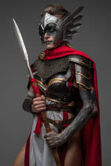 Shot of ancient valkyrie with make up dressed in dark armor with red cape holding spear.