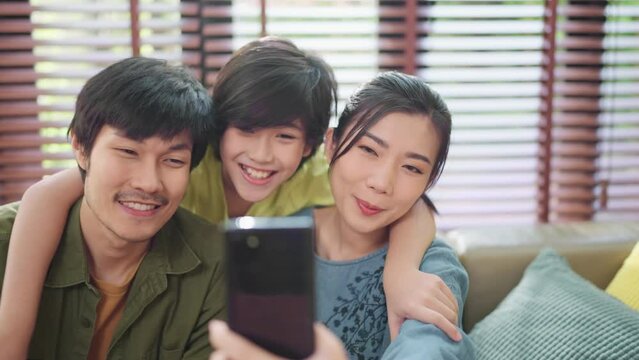 happiness joyful family love concept Asian family holiday activity dad holding smartphone taking a selfie photo together mom son and dad in the living room home interior background