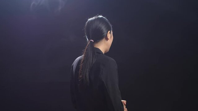 Back View Of Asian Speaker Woman In Business Suit Showing Index Fingers Up While Speaking In The Black Screen Studio
