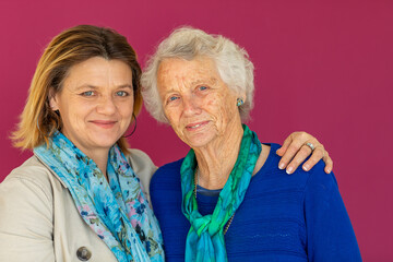 middle-aged woman with her elderly mother against pink background