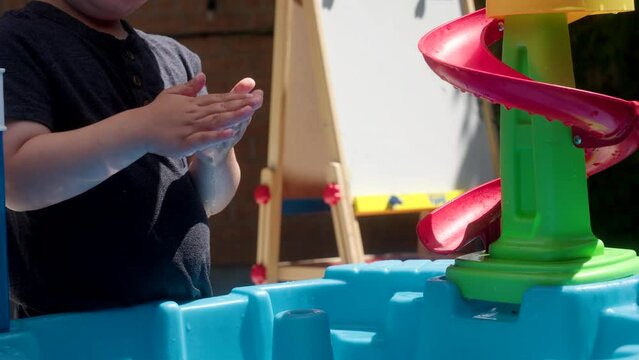 A boy washing his hands in a water table.