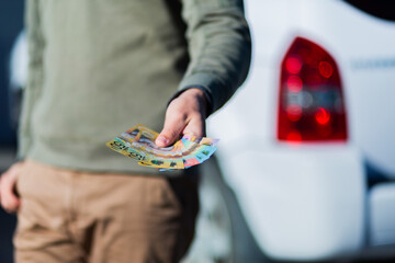 Young man holding cash standing in front of car paying up front
