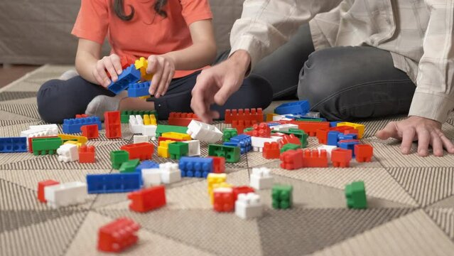 Developing game with constructor. A child play with her dad with plastic colorful blocks in the room.