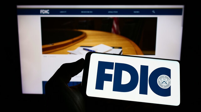 Stuttgart, Germany - 07-10-2022: Person holding cellphone with logo of US Federal Deposit Insurance Corporation (FDIC) on screen in front of webpage. Focus on phone display.