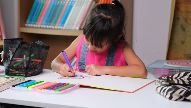 Back to school. Cute little girl holding a magic pen drawing on paper on the table. Asian elementary school girl learning to draw in the classroom.