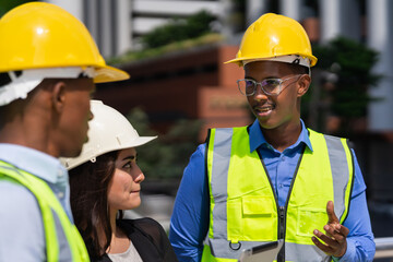 black executive engineer wear helmet working at construction site outside building in city and looking at caucasian businesswoman and black engineer