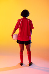 Fototapeta na wymiar Rear view of african american female rugby player with rugby ball over neon yellow lighting