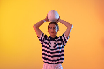 Portrait of caucasian female rugby player with rugby ball over neon yellow lighting