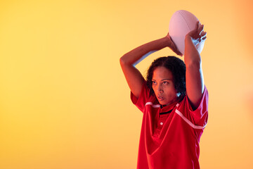 African american female rugby player with rugby ball over neon yellow lighting