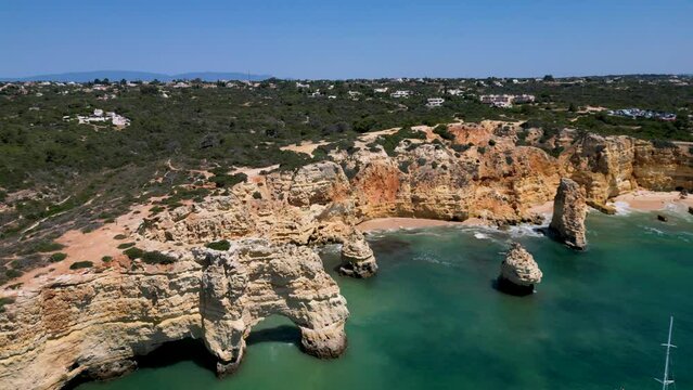 Drone shot on Arco Natural and Praia Marinha. On the ocean, a catamaran and people in canoes. View of the cliffs. Lagoa, Algarve, Portugal