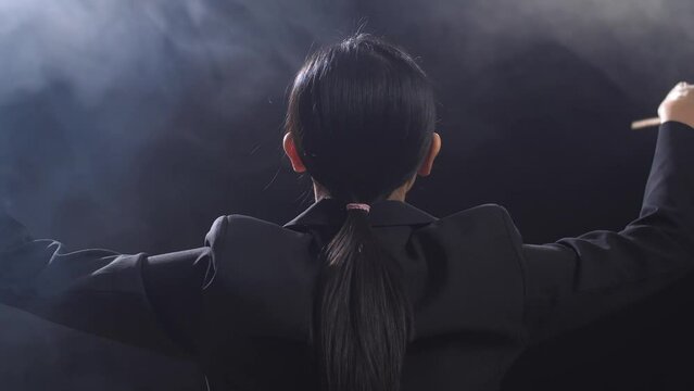 Close Up Of Back View Asian Conductor Woman Holding A Baton And Showing Gesture Quickly In The Black Studio With Fog 
