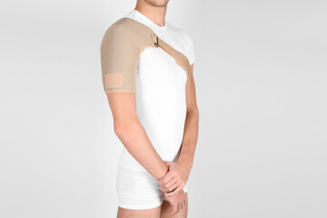 Shoulder joint orthosis or brace isolated on white background. A man in a support orthopedic bandage on his arms after surgery, suffering from shoulder pain, the result of a work injury.
