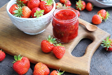 Homemade strawberry jam or marmalade in the glass jar and the fresh strawberries on the wooden...
