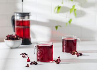 Herbal tea made from hibiscus petals in a transparent cup on a light background and a bowl of dry hibiscus. © Виктория Попова