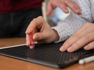 A man teaches a woman how to use a special stencil and stylus to write a letter in Braille.