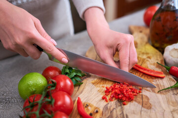 woman cutting and chili pepper by knife on wooden board