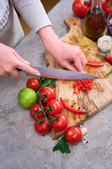 woman cutting and chili pepper by knife on wooden board