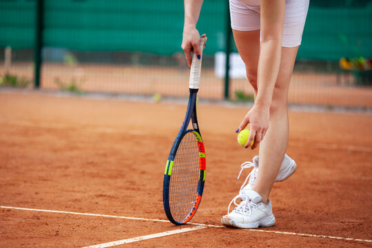 Female tennis player legs in tennis shoes standing on a clay court.