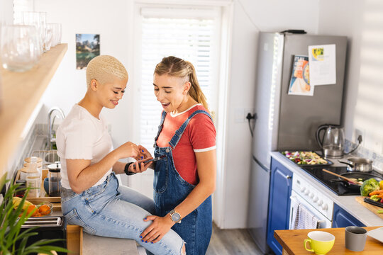 Image of happy diverse lesbian couple talking in kitchen