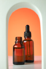 Beauty collagen face serum in a glass dropper bottles in Arch on orange background. Trendy shoot of cosmetics packaging. Essential oil with natural ingredients.