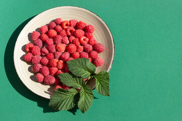 Ripe red raspberries on a round plate on a green background