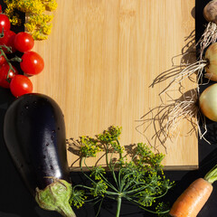 Cutting board surrounded by vegetables and plants: yellow bedstraw flower, red cherry tomatoes, eggplant, dill, carrot, onion, garlic