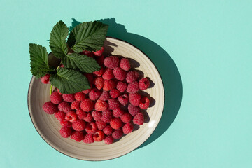 Round plate with raspberries and leaves on a turquoise background