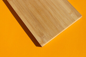 Part of a wooden cutting board on a bright orange background under sunlight
