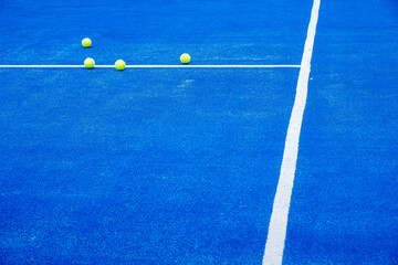 Selective focus. Blue paddle tennis court with synthetic grass and several yellow balls. Racket sports concept